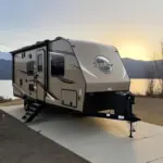 Modern Palomino Solaire travel trailer parked at a scenic campsite overlooking a mountain lake.