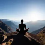 A lone hiker sits meditating on a mountain top, facing the sunrise.