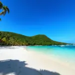 pristine white sand beach with turquoise water and lush green hills in the background