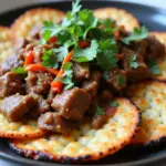 Crispy golden-brown rice crackers topped with tender goat meat in a rich savory sauce